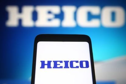 A HEICO logo on a smartphone with a blurred HEICO logo in the background