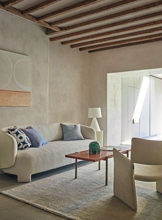 A cream curved sofa in a beige room with exposed wooden beams on the ceiling