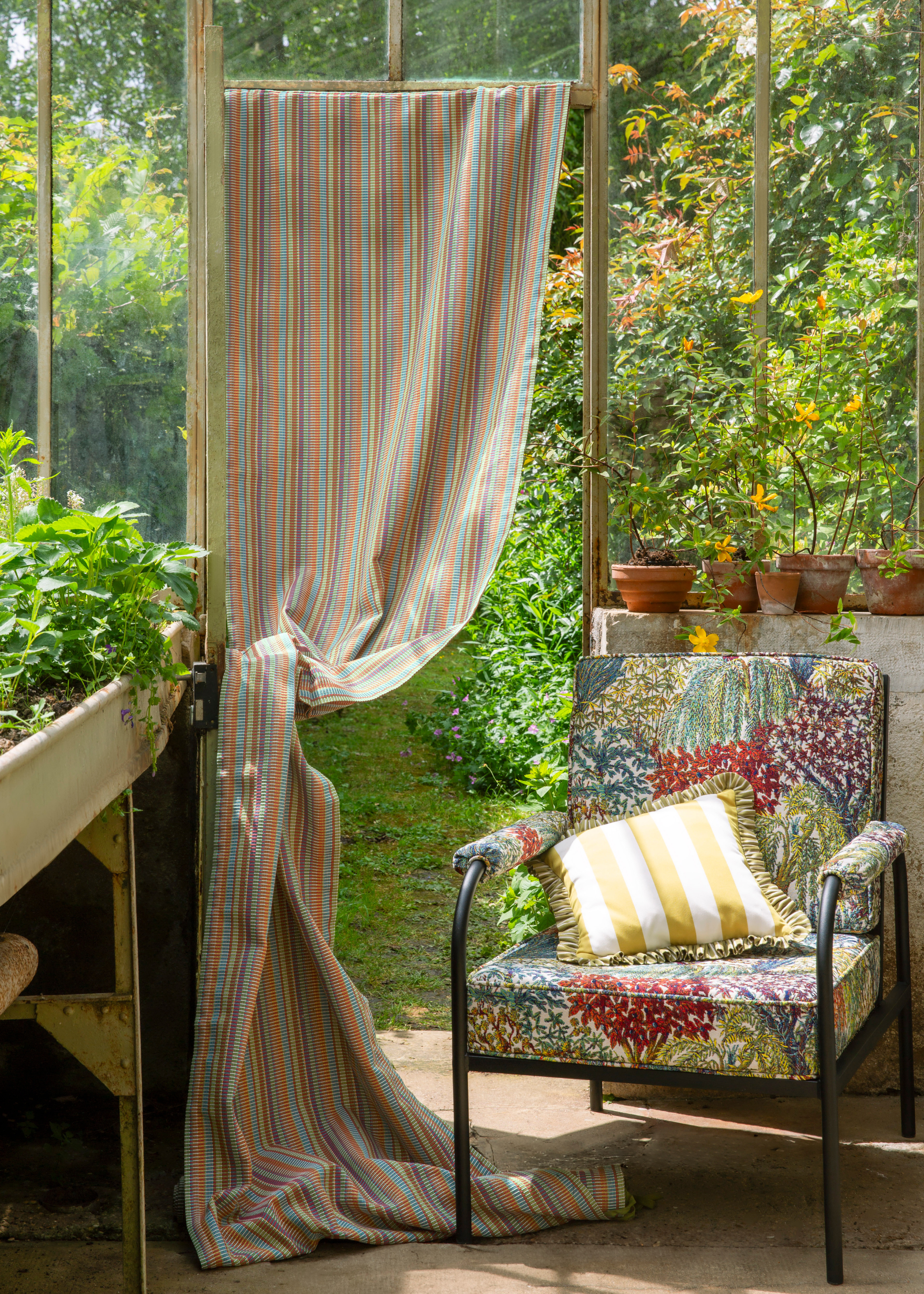 A greenhouse with a curtain door and a striped yellow pillow on a floral chair