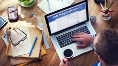 Man holding coffee cup applying for a job on the internet using a laptop