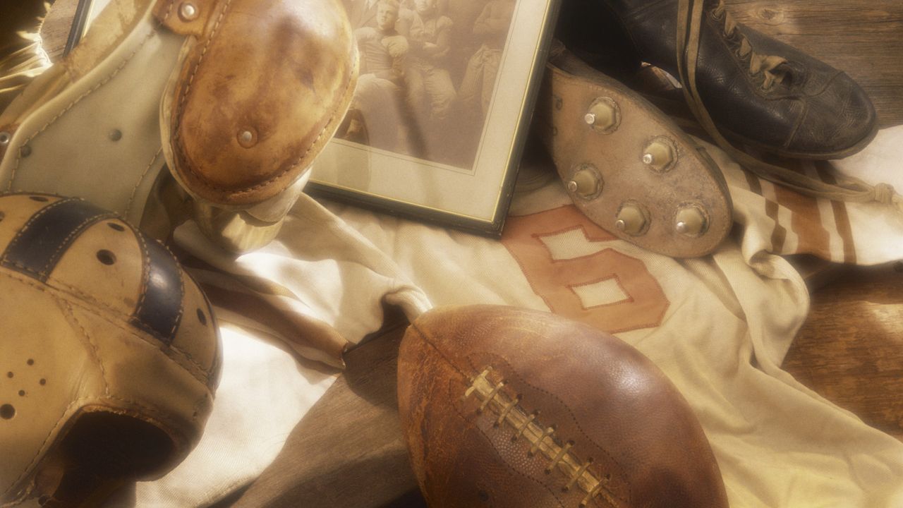 Sports memorabilia such as cleats, a football and a sports jersey are spread over a table.