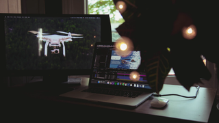 Image of a drone on a monitor next to a MacBook running video editing and VFX software