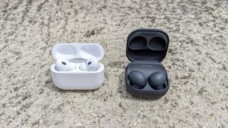 AirPods Pro 2 and Samsung Galaxy Earbuds 2 Pro side-by-side on a wall outside