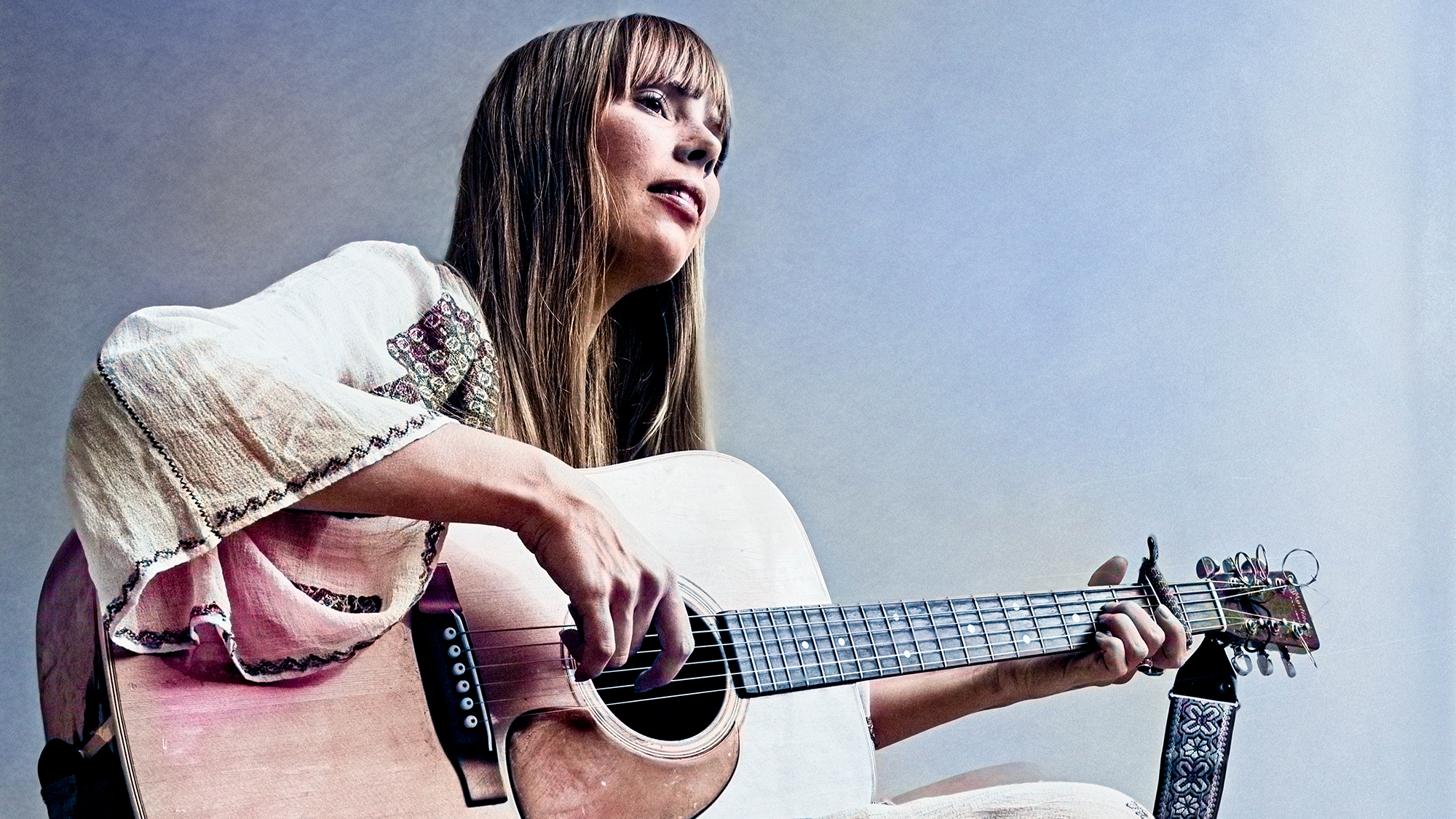 View of Canadian-American Folk musician Joni Mitchell, sitting cross-legged on the floor, as she plays acoustic guitar, New York, New York, November 20, 1968. The photo was taken during a shoot for Vogue magazine. 