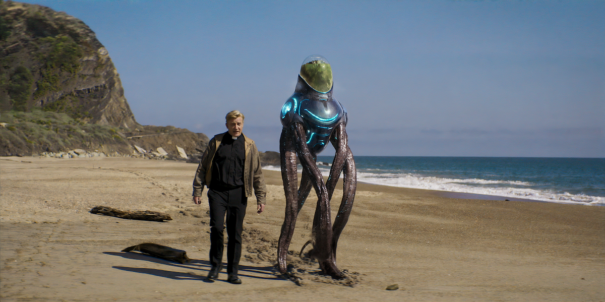 a priest walks with a tentacled alien along the beach