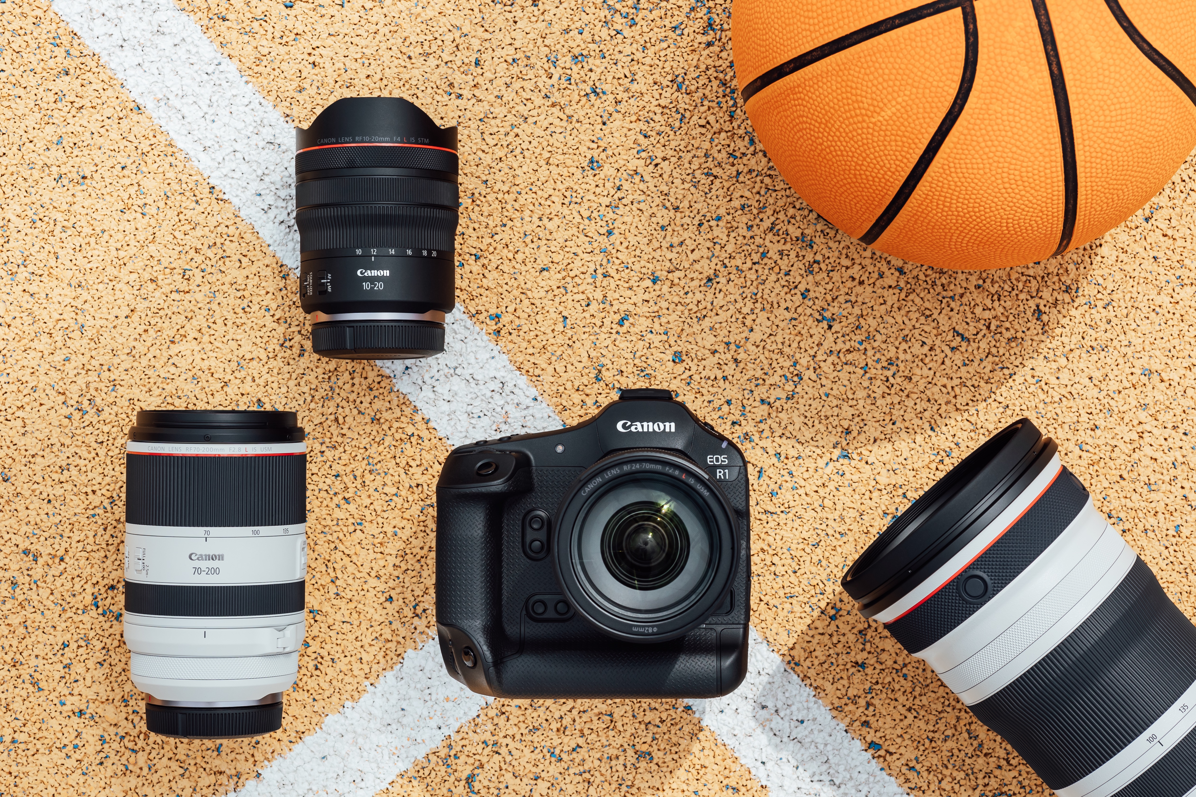 The Canon EOS R1 camera sitting on a court next to a basketball and lenses