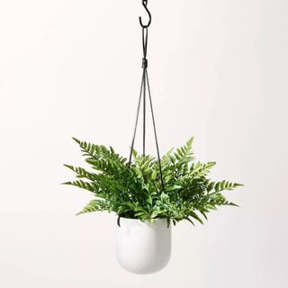 An artificial fern plant hanging in a white pot
