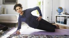 An older woman does yoga in her living room.