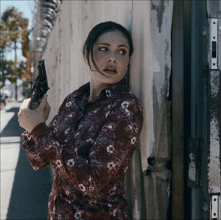 a woman (Juliana Aid&eacute;n Martinez as June Hawkins) hides behind a wall while holding a gun