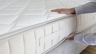 A pair of hands putting a mattress on a mattress foundation
