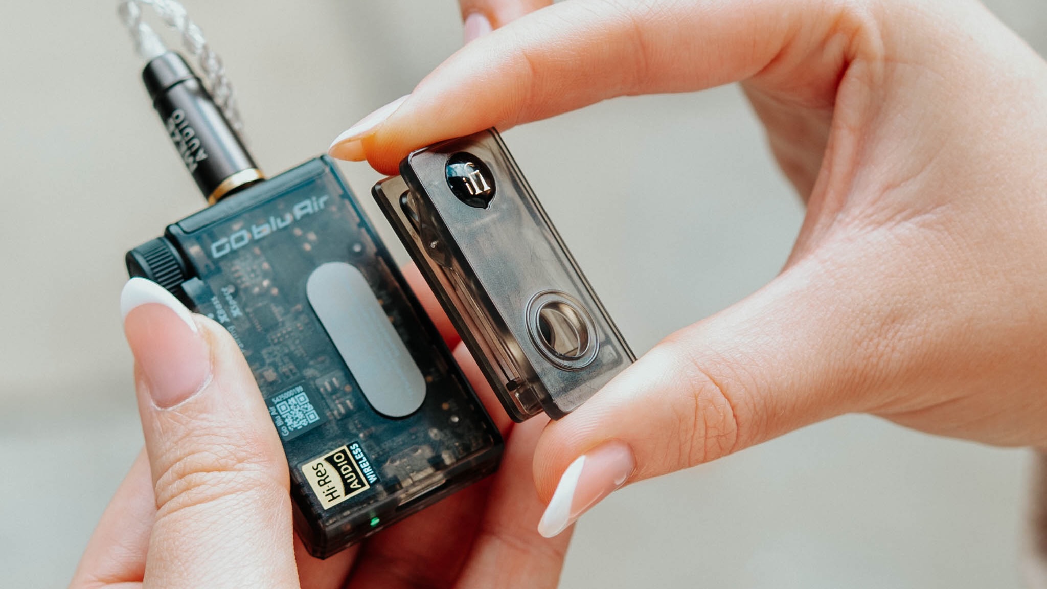 Lifestyle shots showing a model&#039;s hands holding the iFi GO Blu Air portable DAC