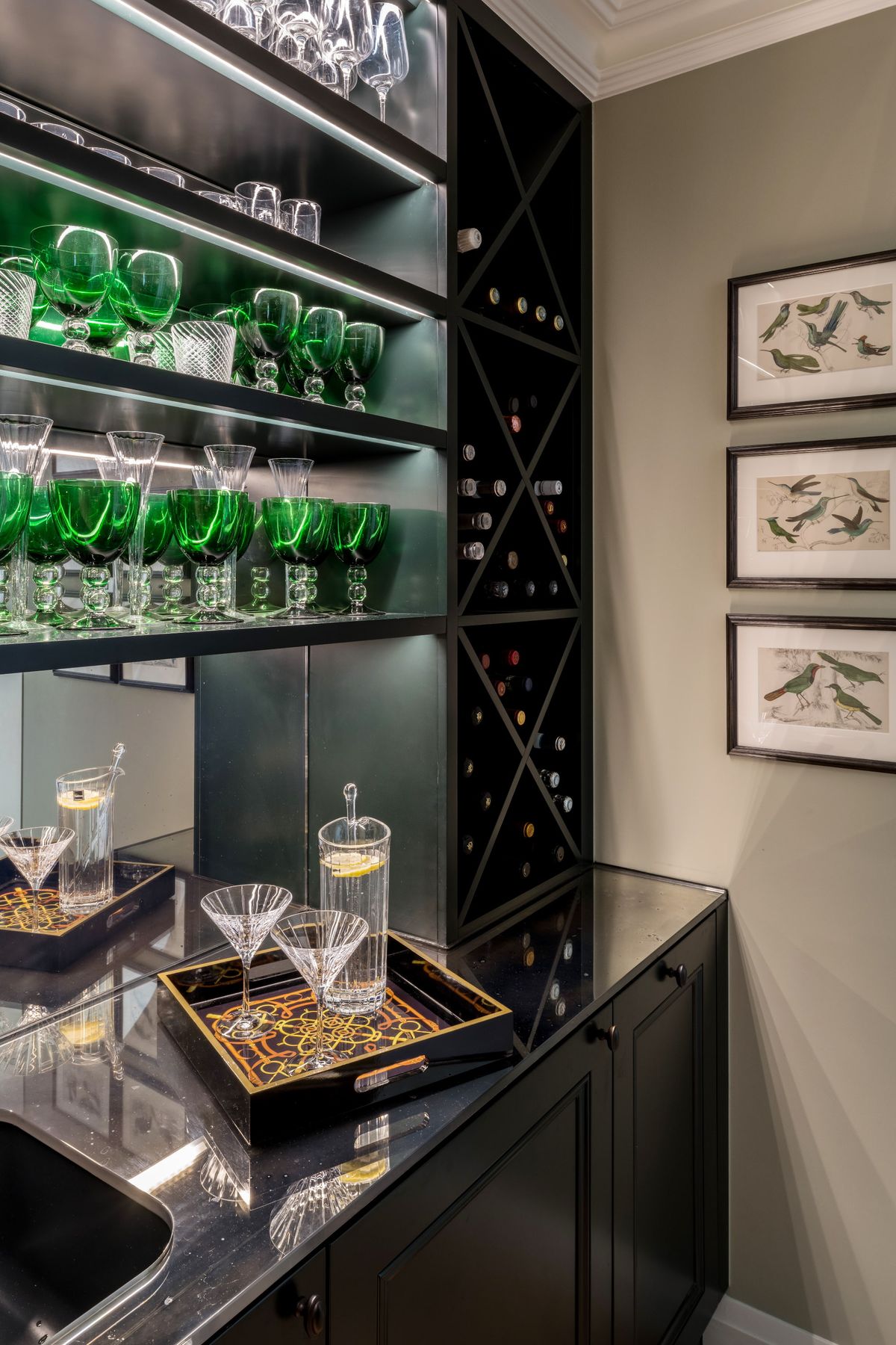 A black built-in cocktail bar unit with mirrored back and green glassware