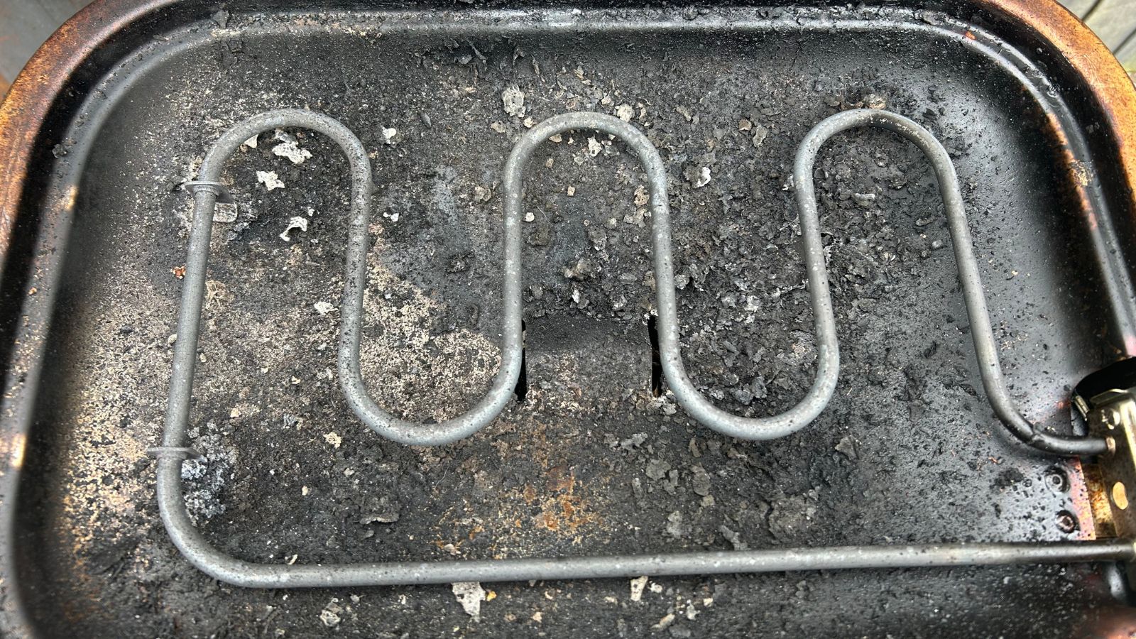 Electric BBQ heating element, sitting atop a dirty bowl with debris