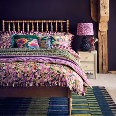 A bedroom with a bobbin bed frame covered with floral bed linen and a ceramic table lamp from the Dunelm x Sophie Robinson collection on the bedside table