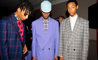 Paul Smith S/S 2019. The model on the left is wearing a blue check jacket with a pink and black scarf, while the model in the middle is wearing a lavender jacket and cap. The guy on the right is wearing a gray check jacket and white shirt.