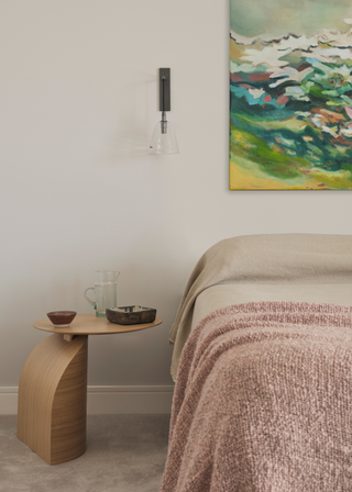 A bedroom with a wooden side table, wall-mounted sconces and hanging art