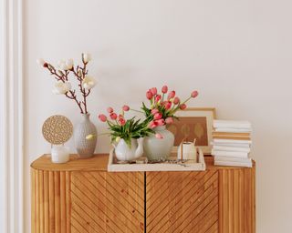 Decor accessories in the interior of a modern bright living room with white walls and wooden furniture. Bouquet of fresh pink tulip flowers.