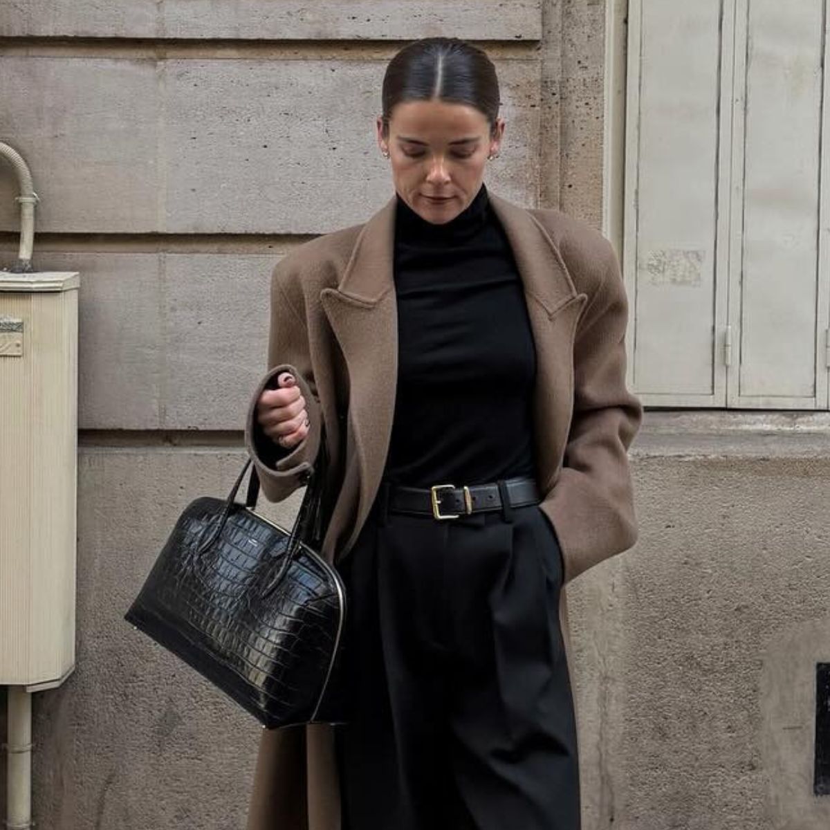 Woman wears mole coat, black turtleneck, black trousers and carries black handbag