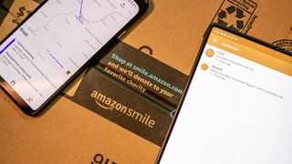 A phone showing Amazon packaging tracking data sits on top of an Amazon package box
