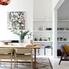 A dining room with the table on top of a berber-style rug with an alcove used for decorative display