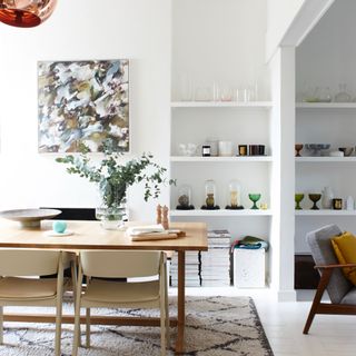 A dining room with the table on top of a berber-style rug with an alcove used for decorative display