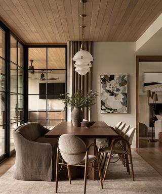 Neutral dining room with wooden table, boucle wood dining chairs, pendant glass lighting, abstract art and wood panelled ceiling