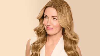 Cat Deeley pictured with long shiny blonde hair, in a white sleeveless top on a beige backdrop