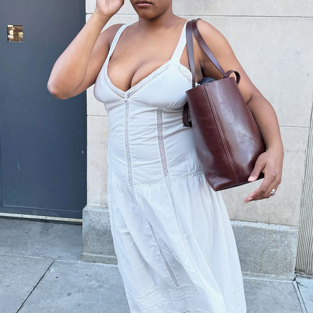 a woman wearing a white dress, brown leather tote bag, and black mary jane flats