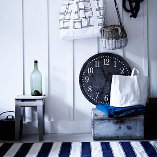 white panelled wall with a black clock wooden stool and a blue and white striped rug on the floor