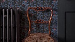 A dark eco-friendly floral wallpaper with a radiator, chair and door