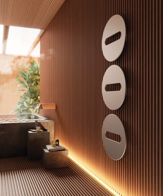 wooden slatted walls and floor with modern brushed steel circular heated radiator panels on wall and built in concrete style bath with waterfall tap