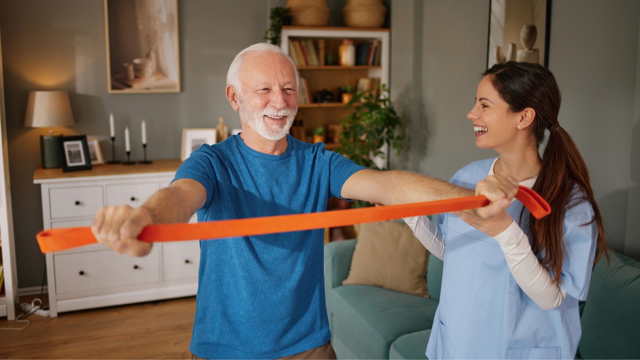 Senior man holding resistance band in front of him under the instruction of a woman wearing a medical smock