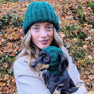 Woman wearing a green knitted hat, holding her dog who is wearing a matching one