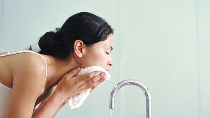 woman washing face with cloth over sink