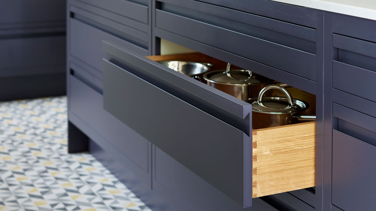 Open drawer in a blue kitchen showing pots and pans