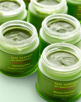 A face mask packaged in a green glass jar with a golden lead features writing which reads "TATA HARPER NEXT GENERATION BEAUTY" and "Clarifying Mask Powered by AHA & BHA" in yellow.