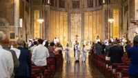Three clergy walking down the aisle of a well lit church.