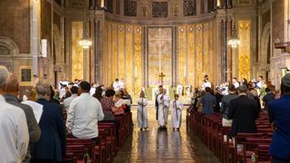 Three clergy walking down the aisle of a well lit church.