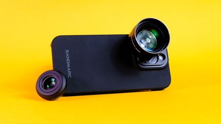 A photo of a Sandmarc iPhone lens attached to an iPhone 15 Pro using the Sandmarc iPhone case, all against a yellow background