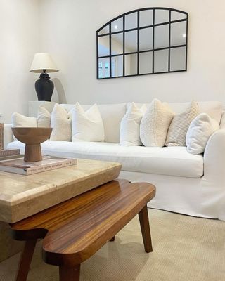 White living room with stone coffee table and solid wood stool addition in front of white fabric couch with arch mirror above