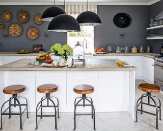 White kitchen ideas with a gray wall, breakfast bar with wooden seating and statement black pendant lights.