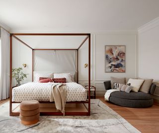 bedroom with white walls and simple four poster bed frame and corner sofa