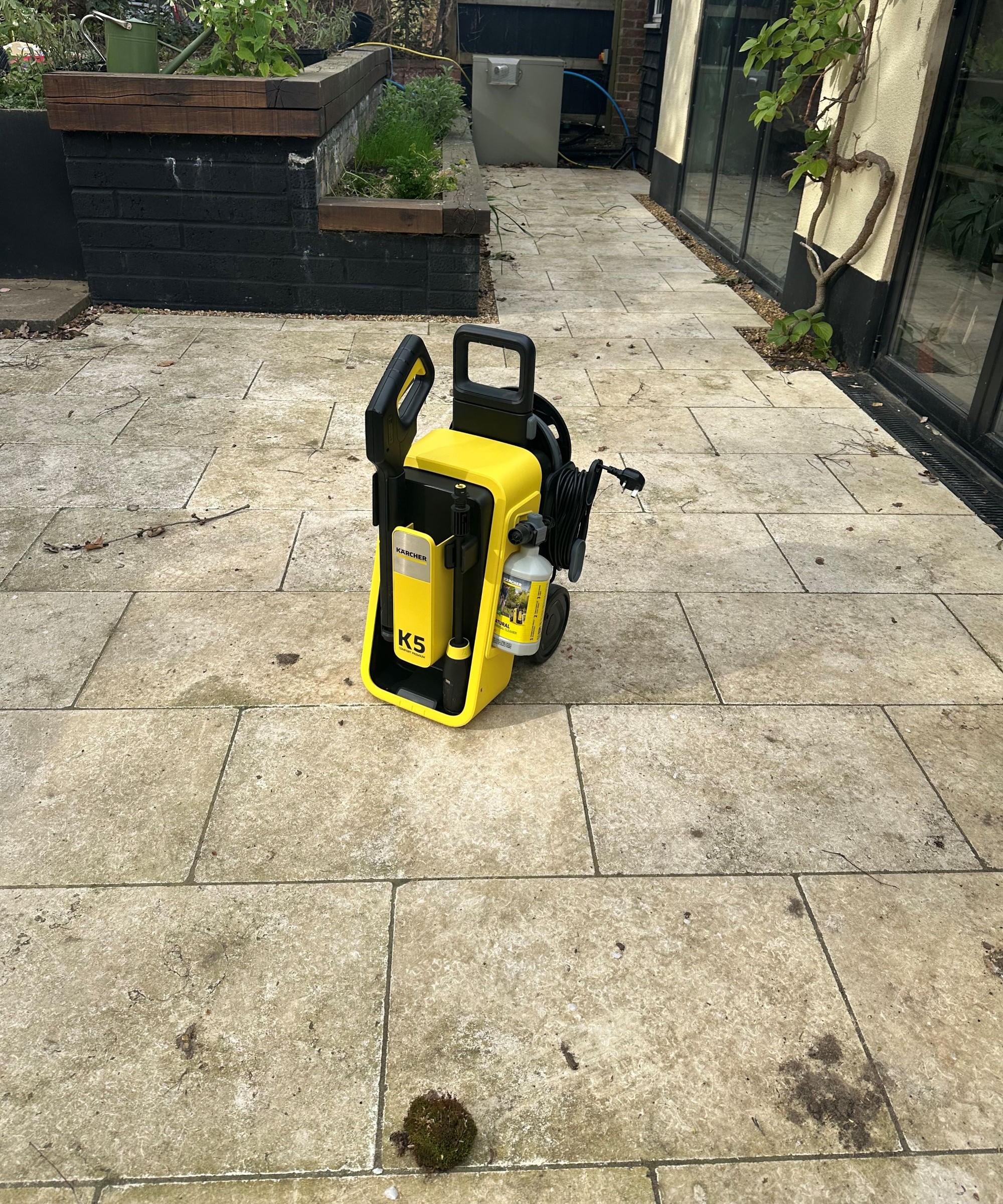 A yellow K&auml;rcher K5 Comfort Premium pressure washer on a cream limestone patio