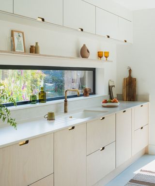 White kitchen with pale wooden cabinets, white worktops and gold accents