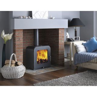 Fire in woodburning stove in facebrick fireplace in living room with grey walls