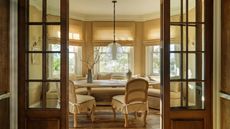 cozy warm beige breakfast nook in a bay window with wooden antique french doors, yellow blinds, two dining chairs with scalloped upholstered seats