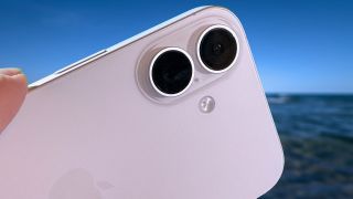 Close up of the cameras on an iPhone 16 held out in front of a blue sky and ocean