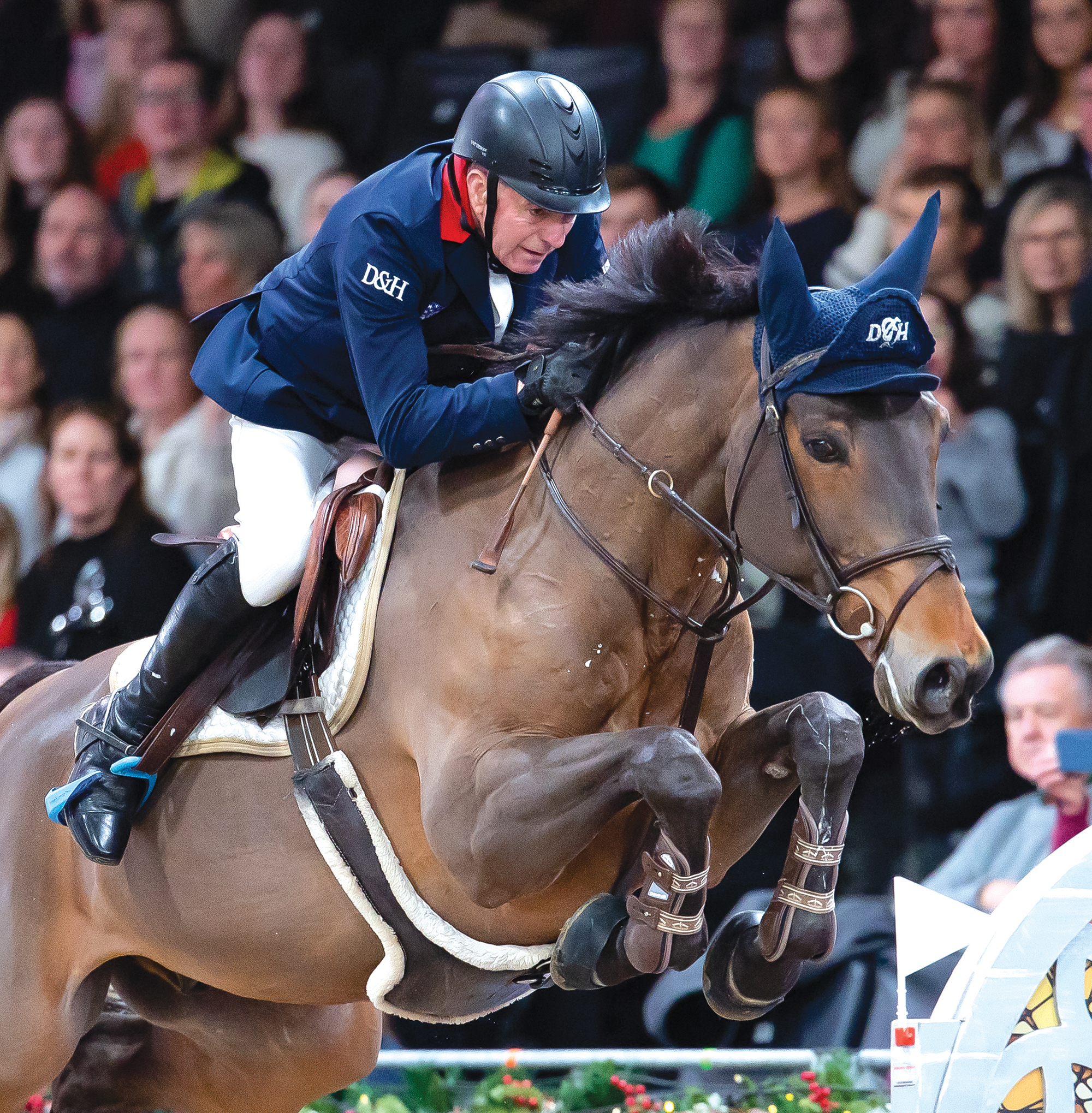 John Whitaker crouches over his horse's neck as they jump a large fence at London International
