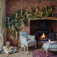 Christmas living room with stove fireplace, bare brick wall, natural fire swag over decorated with ribbons and traditional armchair