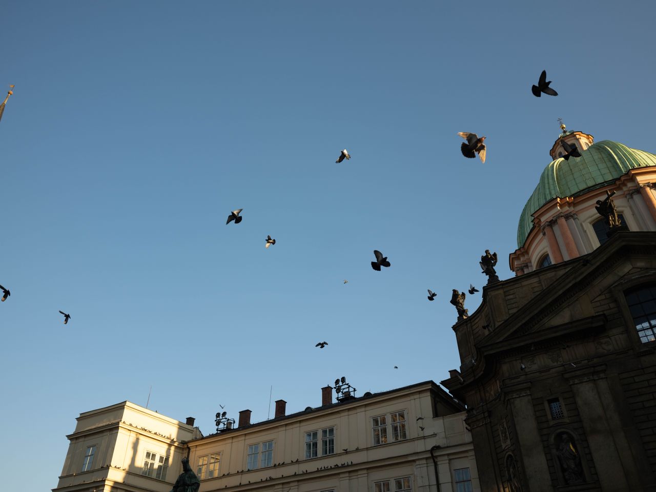 Birds flying across a blue sky in front of an dome of a church in Prague